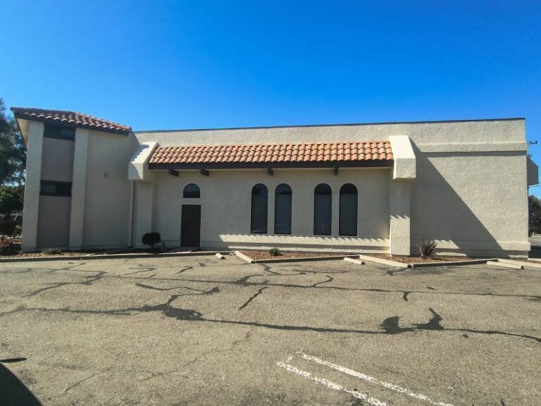 Freshly painted beige exterior of a commercial stucco building with terracotta roof tiles under a clear blue sky