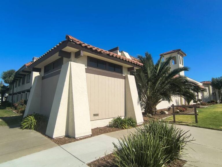 Exterior of a Mediterranean-style commercial building with freshly painted cream stucco, brown wooden trim, and red terracotta roof tiles under a blue sky.
