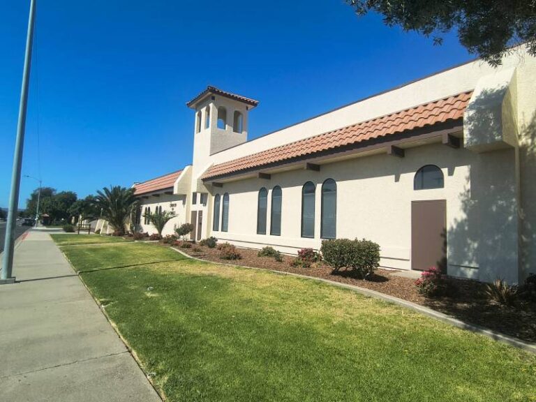 Exterior view of a newly painted commercial stucco building with a tiled roof accent and neat landscaping.