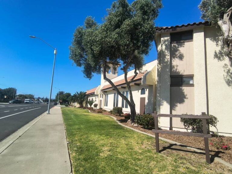 Exterior view of a commercial building with newly painted cream stucco walls and brown trim alongside a sidewalk.