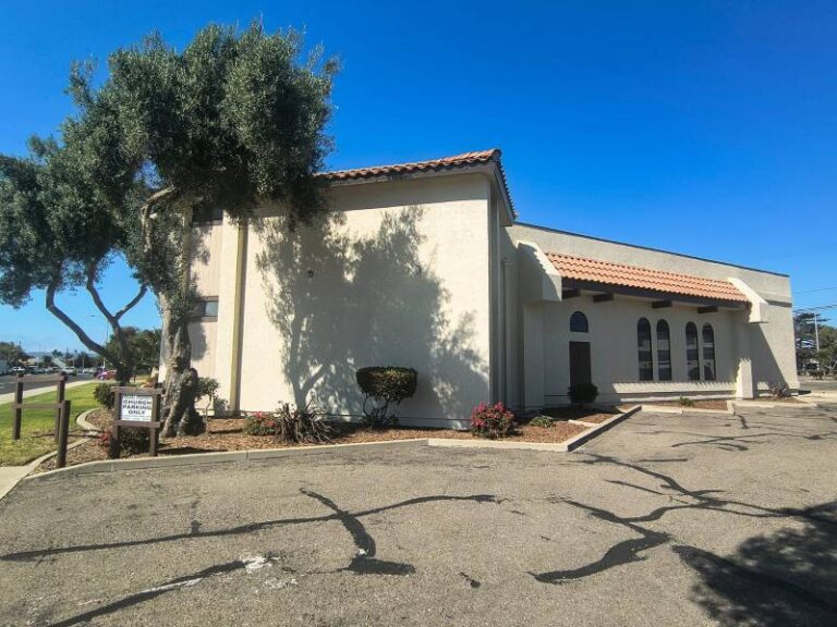 Exterior view of a newly painted off-white stucco commercial building with terracotta roof accents under a clear blue sky.