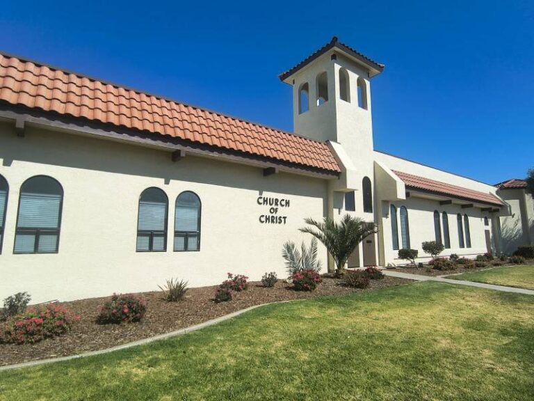Exterior view of a Church of Christ building with freshly painted off-white stucco walls and red Spanish roof tiles.