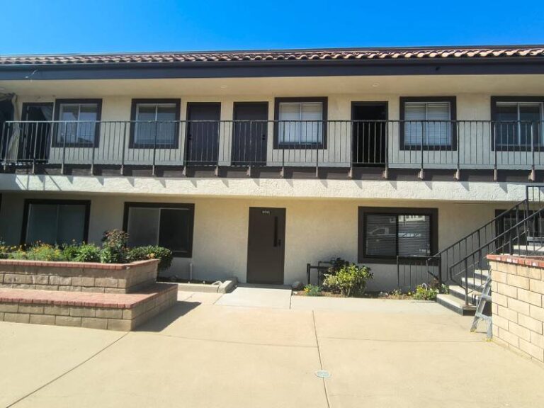 Exterior view of a freshly painted two-story apartment complex featuring clean beige stucco walls and dark brown trim around windows and doors.