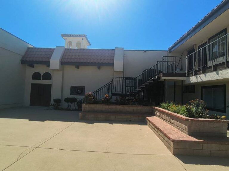 Freshly painted off-white exterior walls of a building complex featuring dark trim, Spanish tile roof accents, black metal stair railings, and a concrete courtyard.