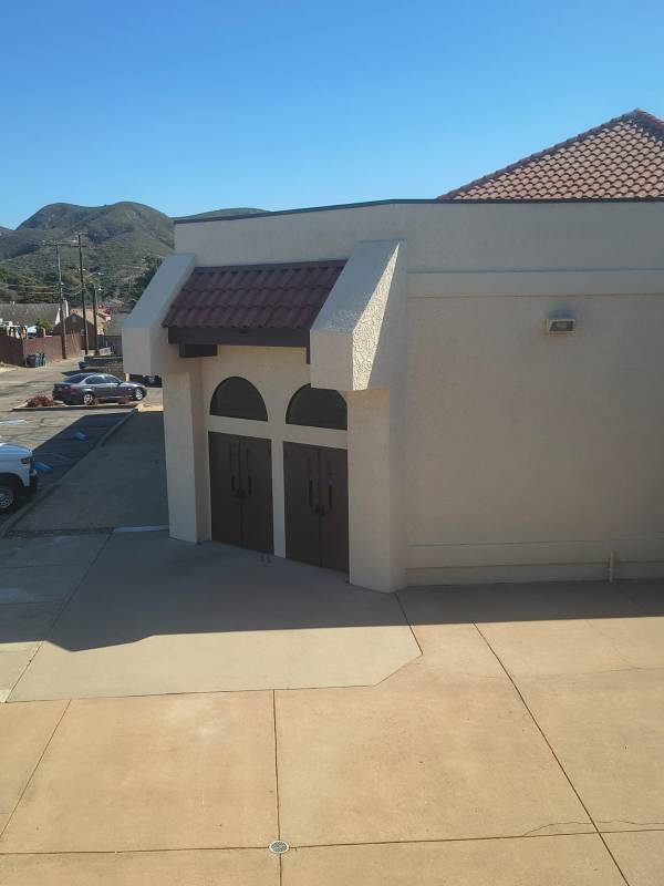 Newly painted beige stucco exterior of a commercial building featuring arched dark wood double doors and a Spanish-style clay tile roof accent.