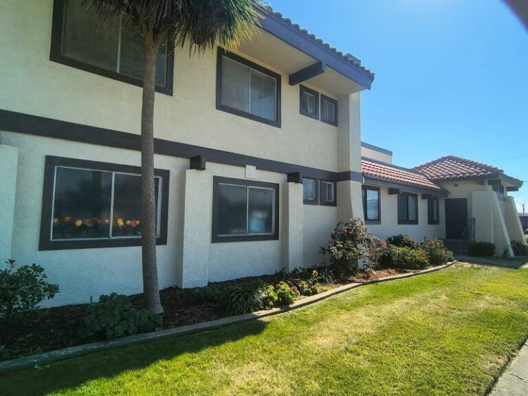 Exterior view of a freshly painted two-story stucco building with off-white walls and dark brown trim around windows and fascia.