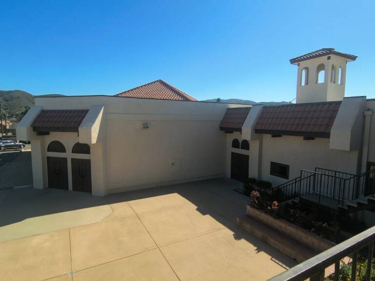 Exterior view of a Spanish-style commercial building with freshly painted cream stucco walls and terracotta roof tiles.