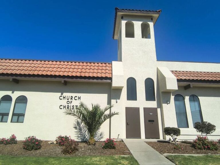 Exterior view of a church building showcasing freshly painted off-white stucco walls, terracotta roof tiles, and dark brown double doors by Hernandez Quality Paint.
