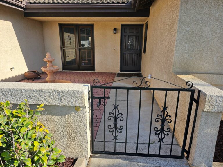Exterior courtyard entryway featuring freshly painted beige stucco walls, dark brown trim, and a black wrought iron gate.