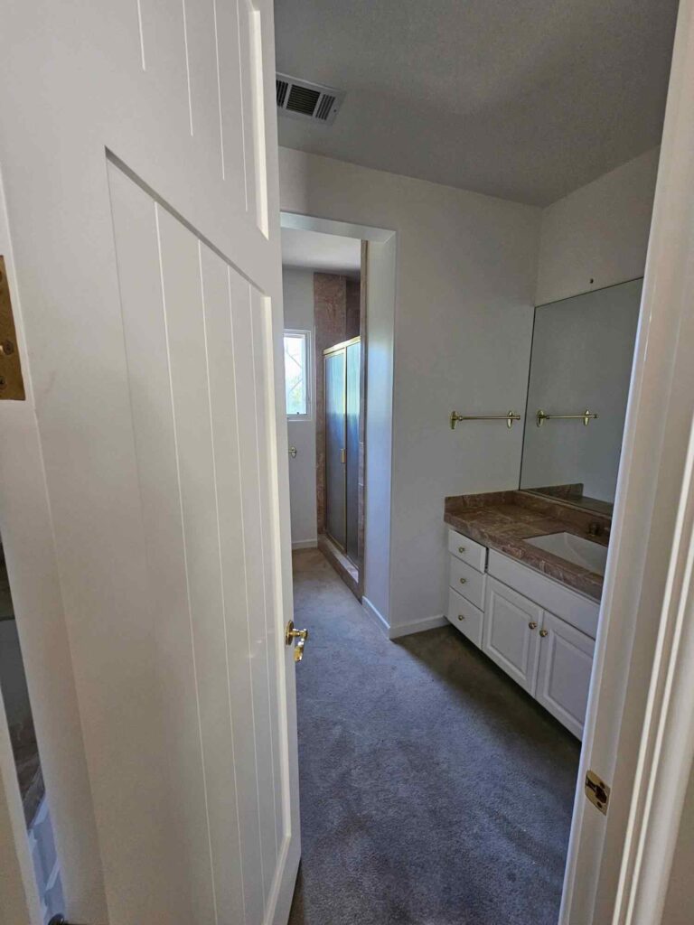 View into a freshly painted bathroom featuring a white vanity with a brown marble countertop, a large mirror, and a glass shower stall, seen from a doorway.