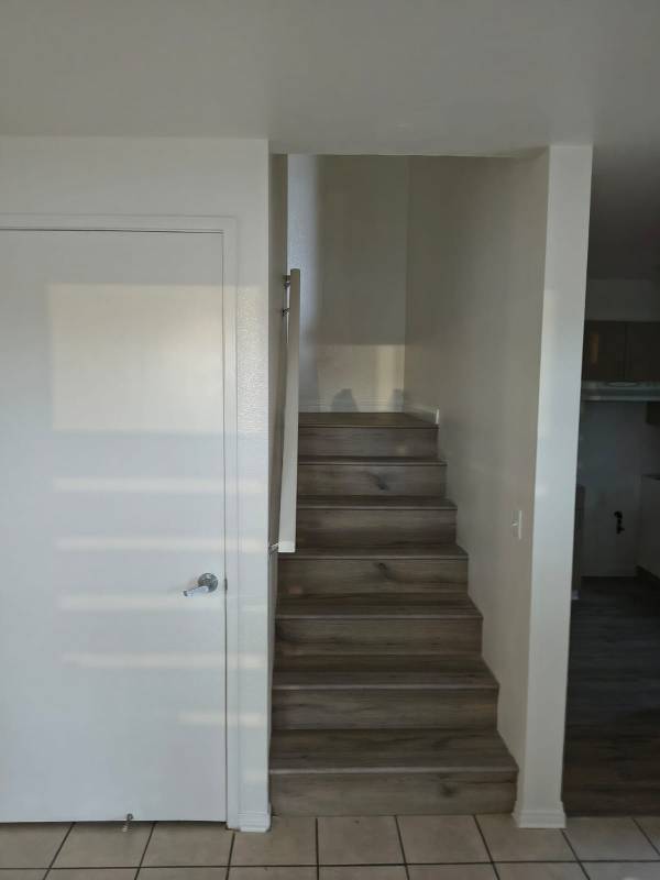 A freshly painted white wall next to a wooden staircase, with a white door on the left and tiled flooring. The wall appears clean and bright, showcasing quality paintwork.